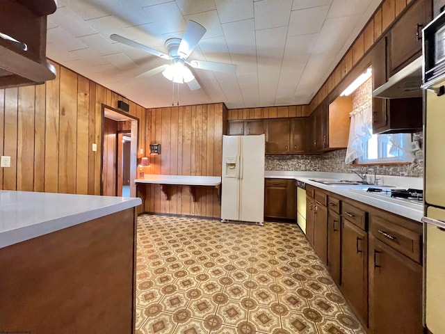 kitchen with white appliances, backsplash, sink, wooden walls, and ceiling fan