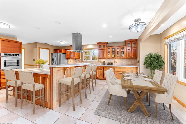 kitchen with stainless steel appliances, tasteful backsplash, a kitchen bar, island range hood, and light tile patterned floors