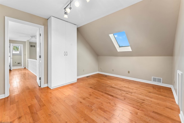 additional living space with lofted ceiling with skylight, light hardwood / wood-style flooring, and ceiling fan