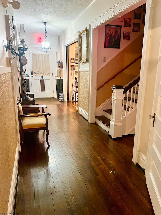 hallway featuring a textured ceiling, dark wood-type flooring, and an inviting chandelier