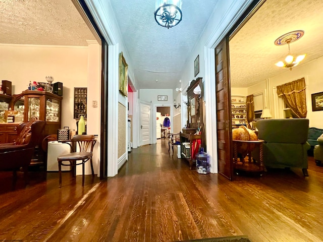 hall with a chandelier, a textured ceiling, hardwood / wood-style flooring, and ornamental molding