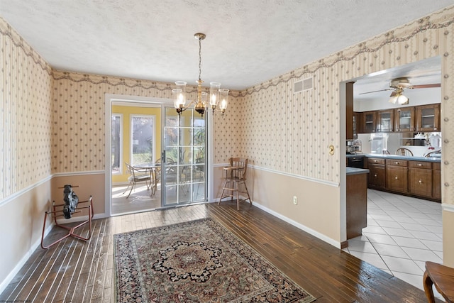 dining area with hardwood / wood-style flooring, ceiling fan with notable chandelier, and a textured ceiling