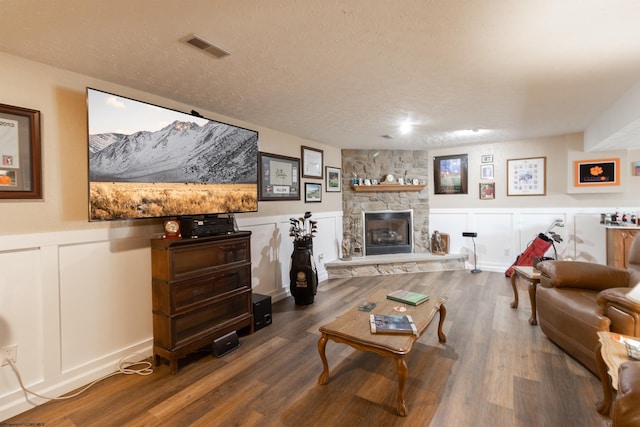 living room with hardwood / wood-style floors, a textured ceiling, and a stone fireplace