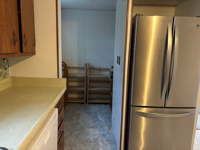 kitchen featuring white dishwasher, wood walls, and stainless steel refrigerator