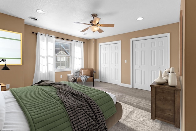 bedroom with ceiling fan, light colored carpet, a textured ceiling, and two closets