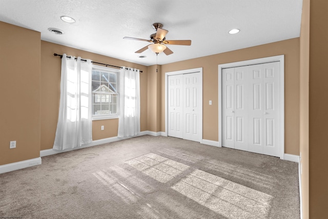 unfurnished bedroom featuring carpet, ceiling fan, a textured ceiling, and multiple closets