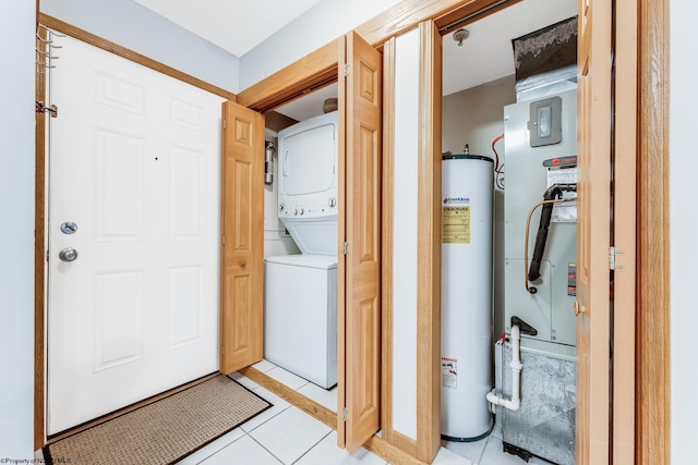 clothes washing area featuring light tile patterned flooring, stacked washing maching and dryer, and water heater