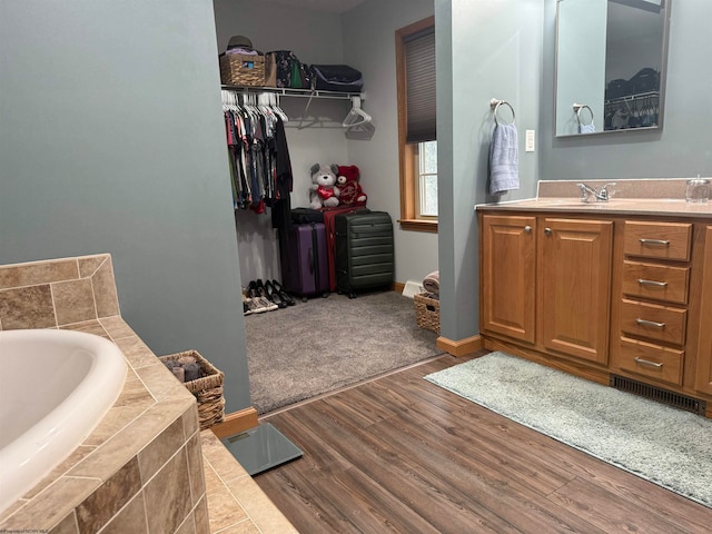 bathroom with hardwood / wood-style flooring, vanity, and a relaxing tiled tub