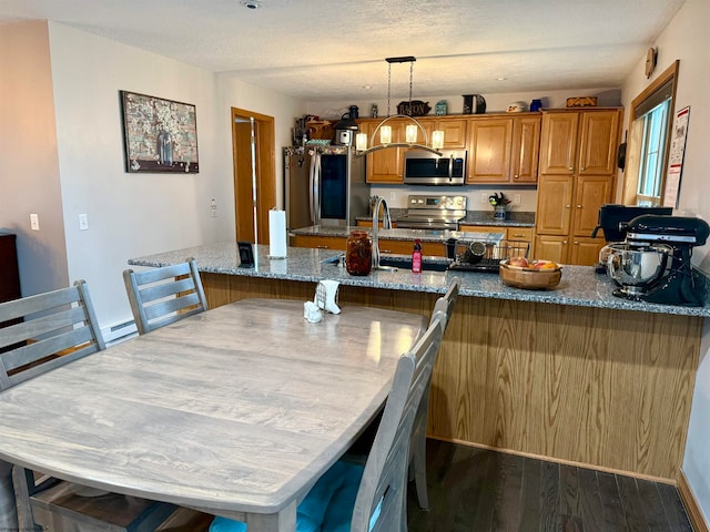 kitchen with dark wood-type flooring, a textured ceiling, decorative light fixtures, light stone counters, and stainless steel appliances