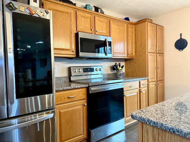 kitchen with dark stone countertops, dark hardwood / wood-style flooring, a textured ceiling, and appliances with stainless steel finishes