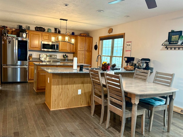 kitchen with a center island, dark wood-type flooring, hanging light fixtures, stone countertops, and stainless steel appliances