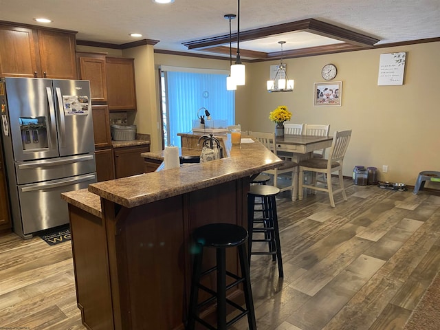 kitchen featuring dark wood-type flooring, crown molding, stainless steel fridge, a breakfast bar, and a center island with sink