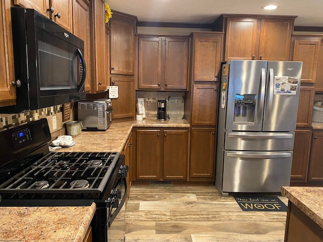 kitchen featuring light stone countertops, light hardwood / wood-style floors, tasteful backsplash, and black appliances