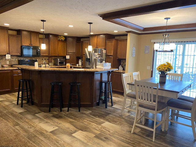 kitchen featuring dark hardwood / wood-style flooring, a kitchen island with sink, black appliances, decorative light fixtures, and a breakfast bar area