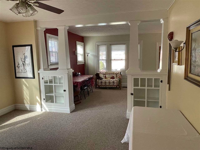 interior space with ceiling fan, carpet floors, a textured ceiling, and decorative columns