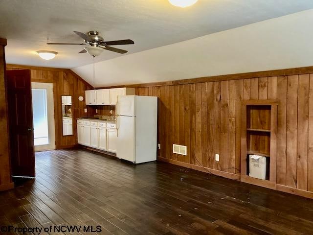 kitchen with lofted ceiling, wooden walls, dark hardwood / wood-style floors, white fridge, and white cabinetry