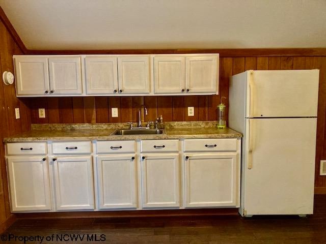 kitchen featuring wood walls, white fridge, dark hardwood / wood-style flooring, and sink