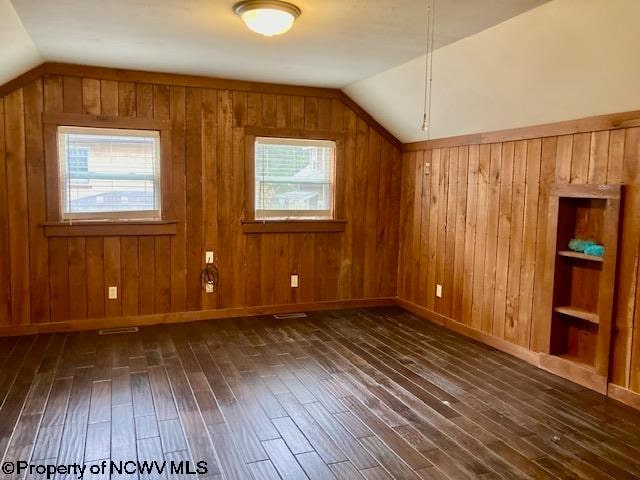 additional living space featuring dark hardwood / wood-style floors, vaulted ceiling, plenty of natural light, and wood walls