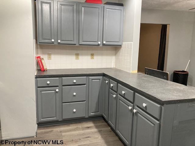 kitchen with kitchen peninsula, light wood-type flooring, gray cabinets, and backsplash