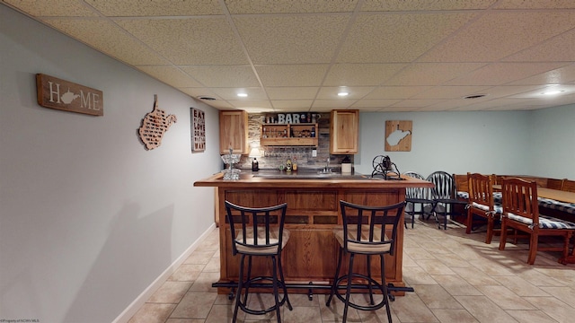 bar featuring light tile patterned floors, a paneled ceiling, and tasteful backsplash