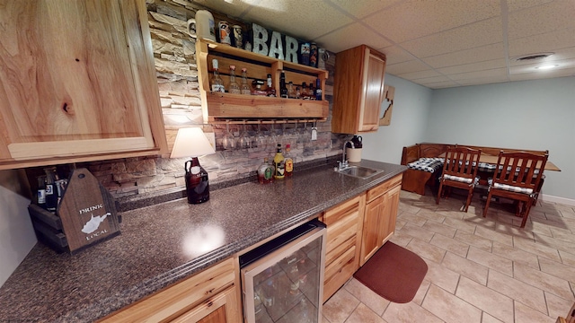 bar featuring a paneled ceiling, sink, tasteful backsplash, light tile patterned flooring, and beverage cooler