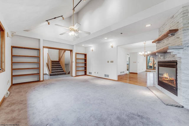 unfurnished living room with carpet floors, track lighting, a stone fireplace, and ceiling fan