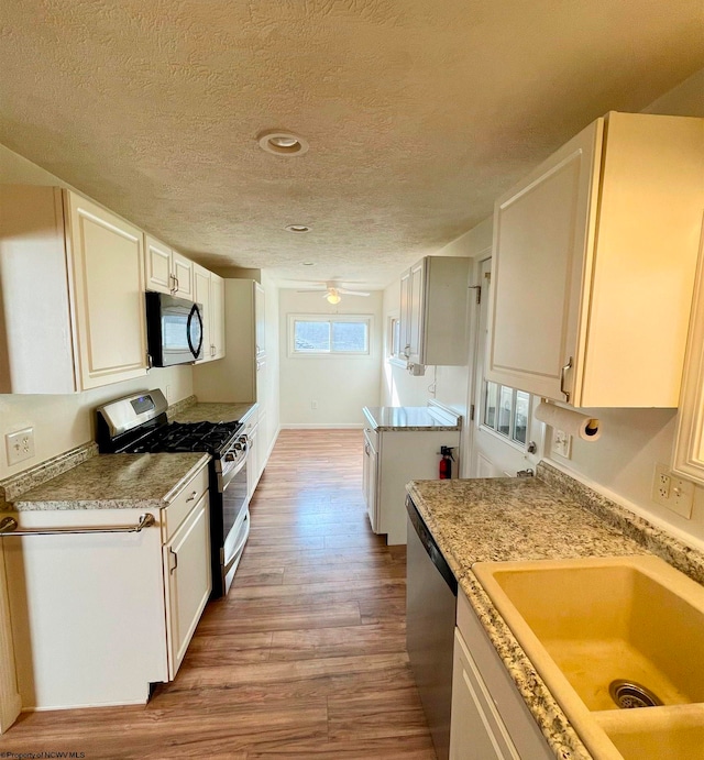 kitchen featuring sink, light hardwood / wood-style floors, a textured ceiling, white cabinets, and appliances with stainless steel finishes