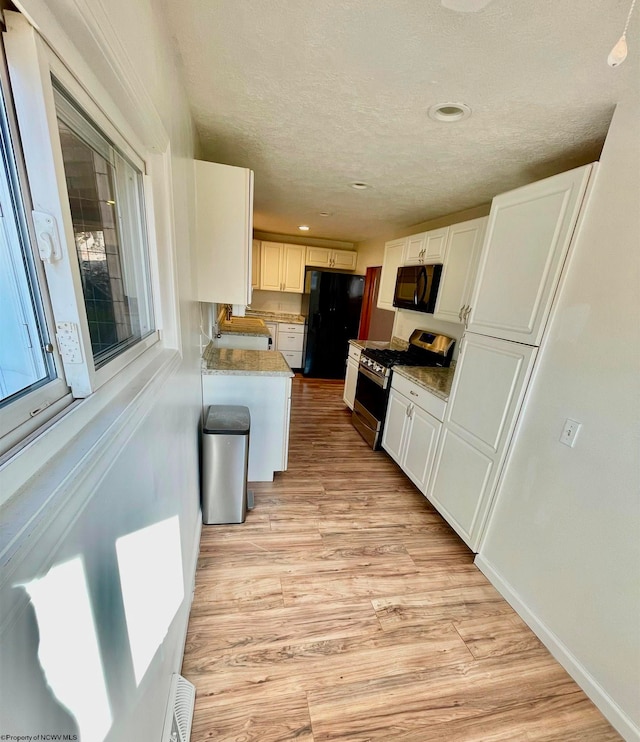 kitchen featuring black appliances, sink, light stone countertops, light hardwood / wood-style floors, and white cabinetry