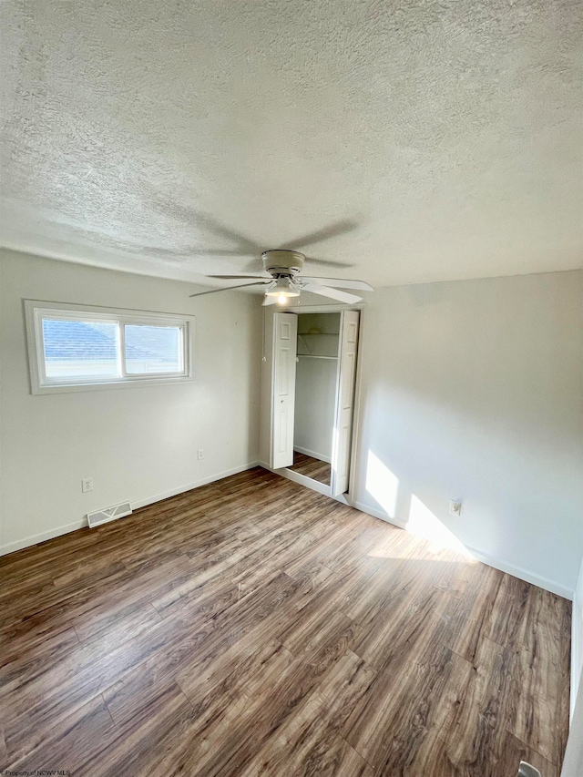 unfurnished bedroom featuring ceiling fan, dark hardwood / wood-style flooring, a textured ceiling, and a closet