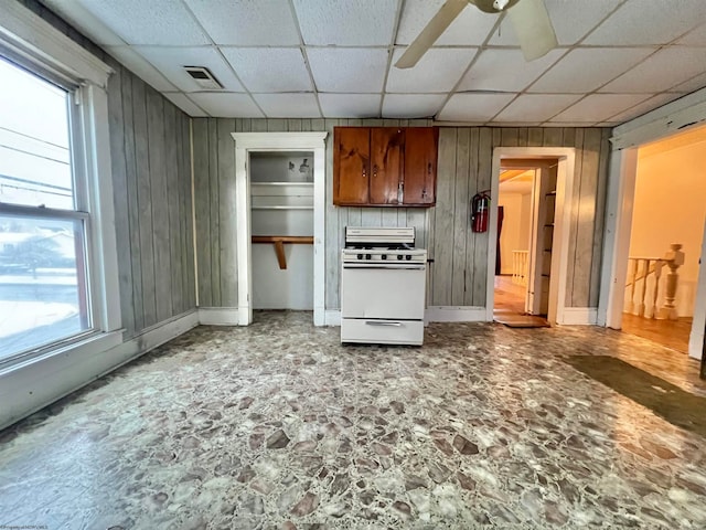 kitchen with a drop ceiling, wood walls, white range oven, and plenty of natural light