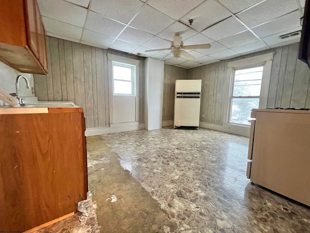 kitchen featuring a drop ceiling, ceiling fan, sink, white fridge, and wood walls