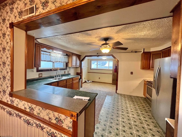 kitchen with a textured ceiling, ceiling fan, sink, and stainless steel refrigerator with ice dispenser