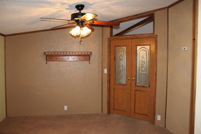 carpeted foyer entrance featuring french doors, a textured ceiling, vaulted ceiling, ceiling fan, and crown molding