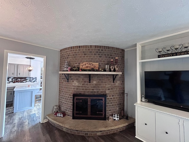 unfurnished living room with ornamental molding, dark wood-type flooring, a textured ceiling, and a brick fireplace