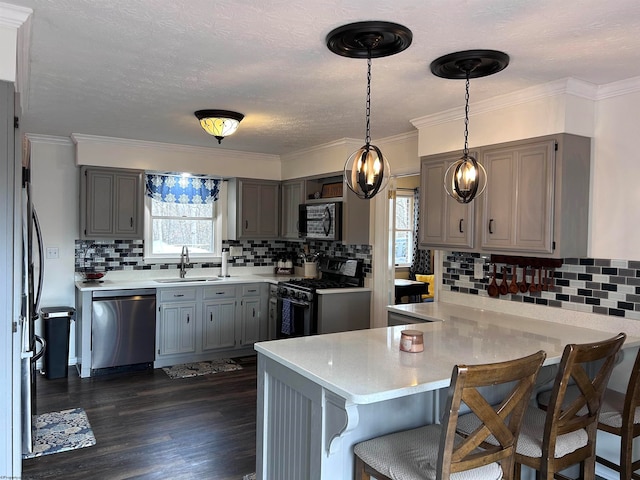 kitchen featuring kitchen peninsula, appliances with stainless steel finishes, sink, pendant lighting, and dark hardwood / wood-style floors