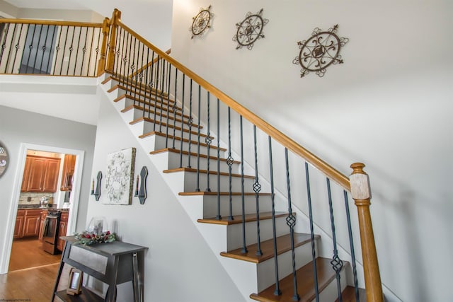 staircase with wood-type flooring and a towering ceiling