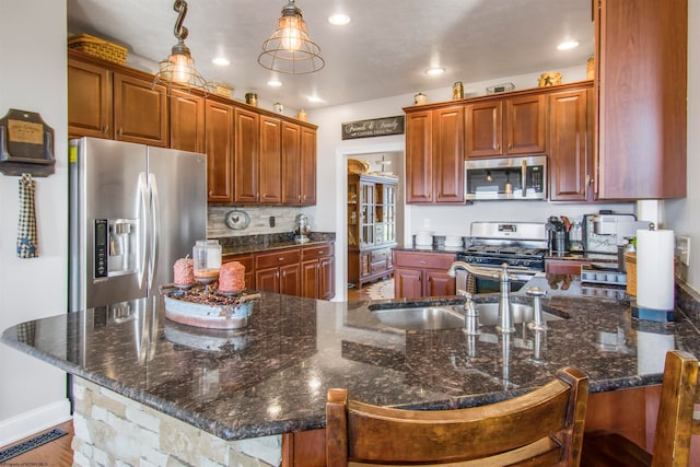 kitchen featuring sink, dark stone countertops, an island with sink, appliances with stainless steel finishes, and decorative light fixtures