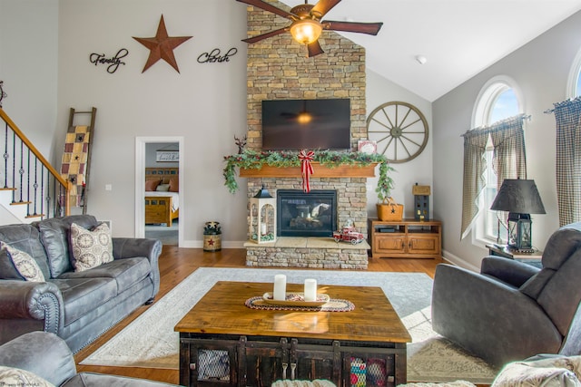 living room featuring ceiling fan, light hardwood / wood-style floors, a stone fireplace, and high vaulted ceiling