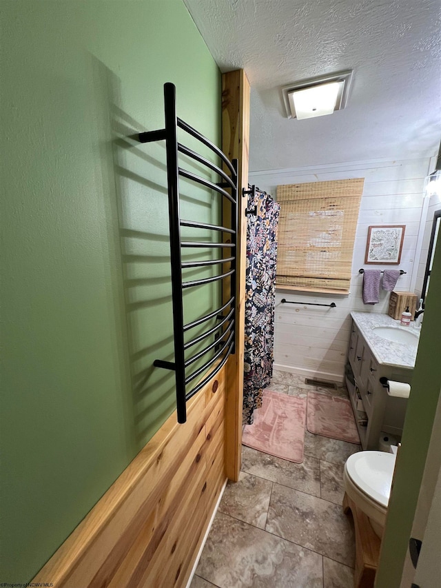 bathroom featuring vanity, toilet, a textured ceiling, and wooden walls