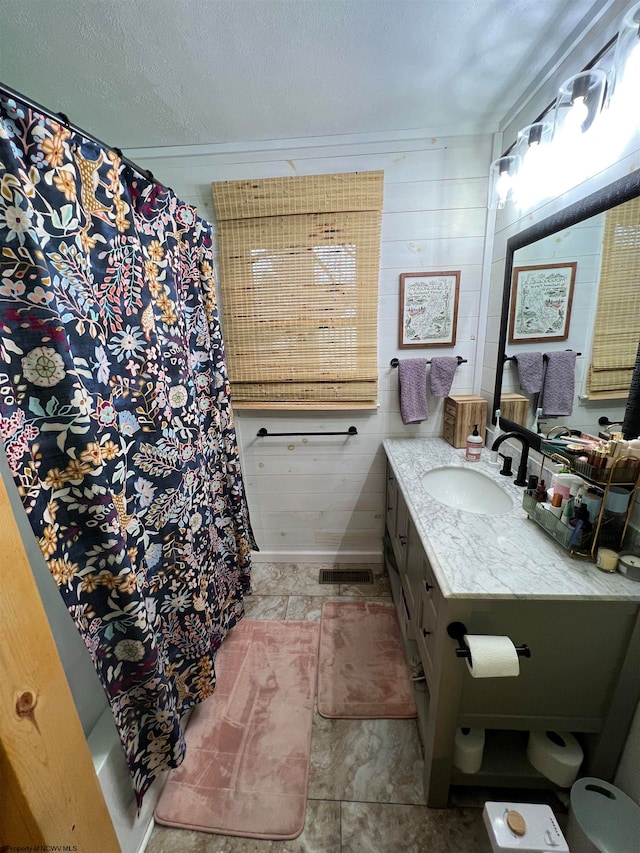 bathroom featuring a textured ceiling, vanity, curtained shower, and wooden walls