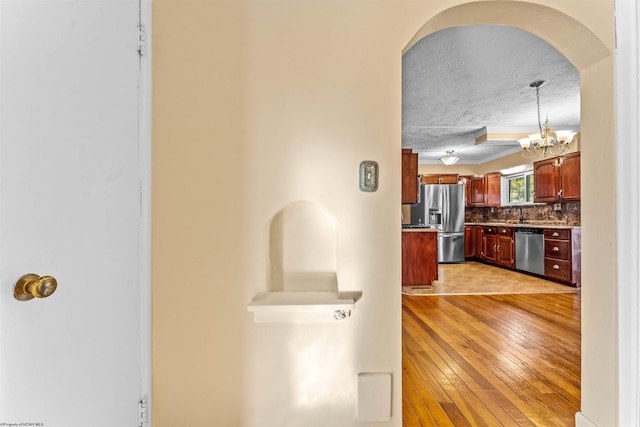 hallway featuring light hardwood / wood-style flooring, a textured ceiling, and an inviting chandelier