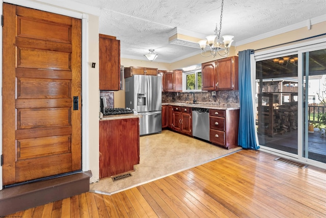 kitchen featuring hanging light fixtures, light hardwood / wood-style flooring, stainless steel appliances, and a textured ceiling