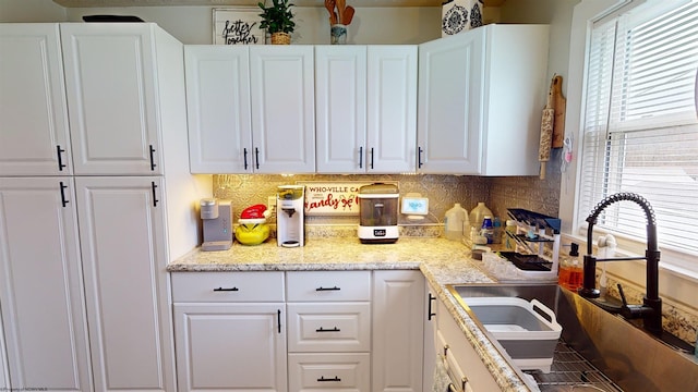 kitchen featuring decorative backsplash, white cabinetry, sink, and light stone counters