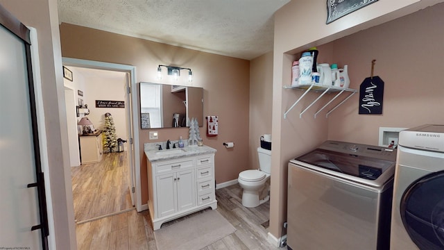 laundry area featuring washing machine and dryer, a textured ceiling, and light hardwood / wood-style flooring