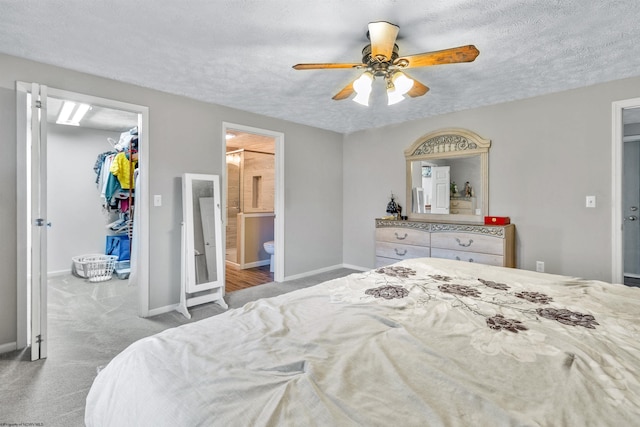 carpeted bedroom with ceiling fan, ensuite bathroom, a walk in closet, and a textured ceiling