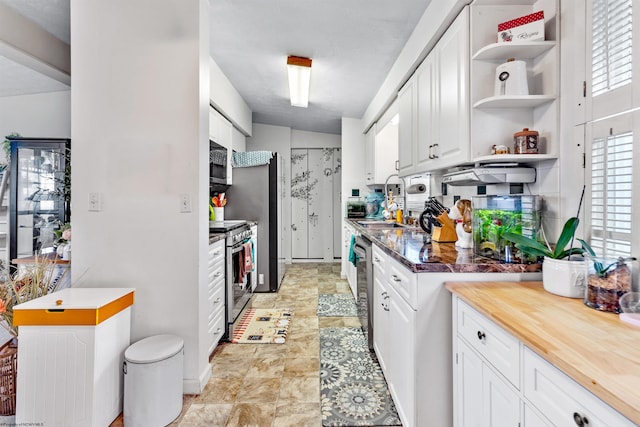 kitchen featuring wood counters, stainless steel appliances, vaulted ceiling, sink, and white cabinets