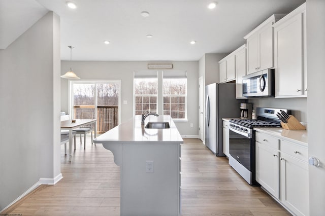 kitchen with sink, light hardwood / wood-style flooring, gas range oven, an island with sink, and white cabinetry