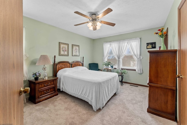 bedroom featuring light carpet, a textured ceiling, and ceiling fan