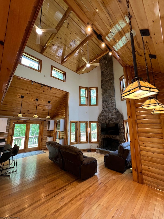 living room featuring beam ceiling, a stone fireplace, high vaulted ceiling, wood ceiling, and light wood-type flooring