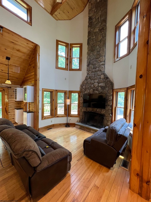 living room with a healthy amount of sunlight, a stone fireplace, wooden ceiling, and high vaulted ceiling